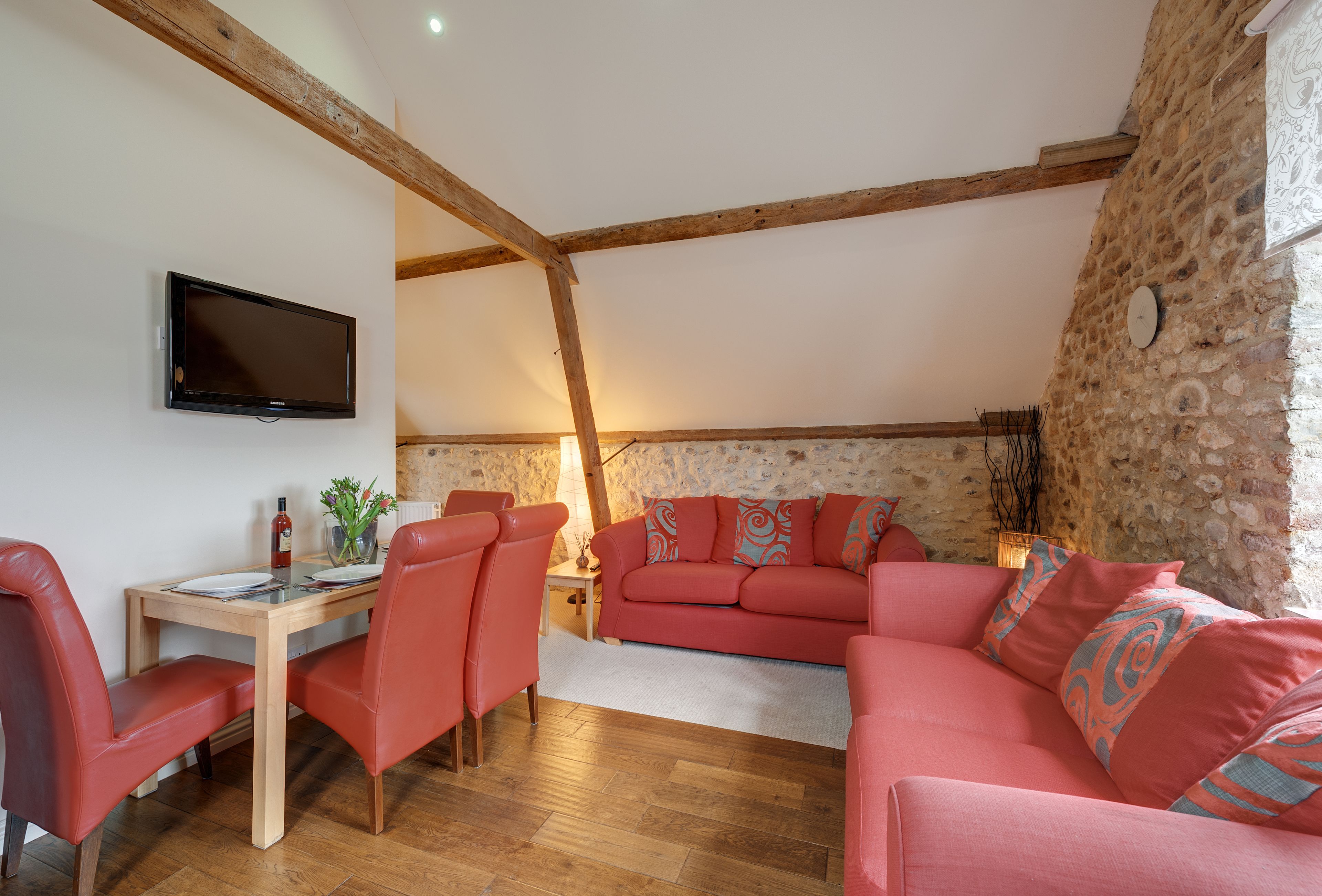 Una sala de estar acogedora con techo de madera, televisor de pantalla plana, sofá rojo y una mesa de comedor con sillas.