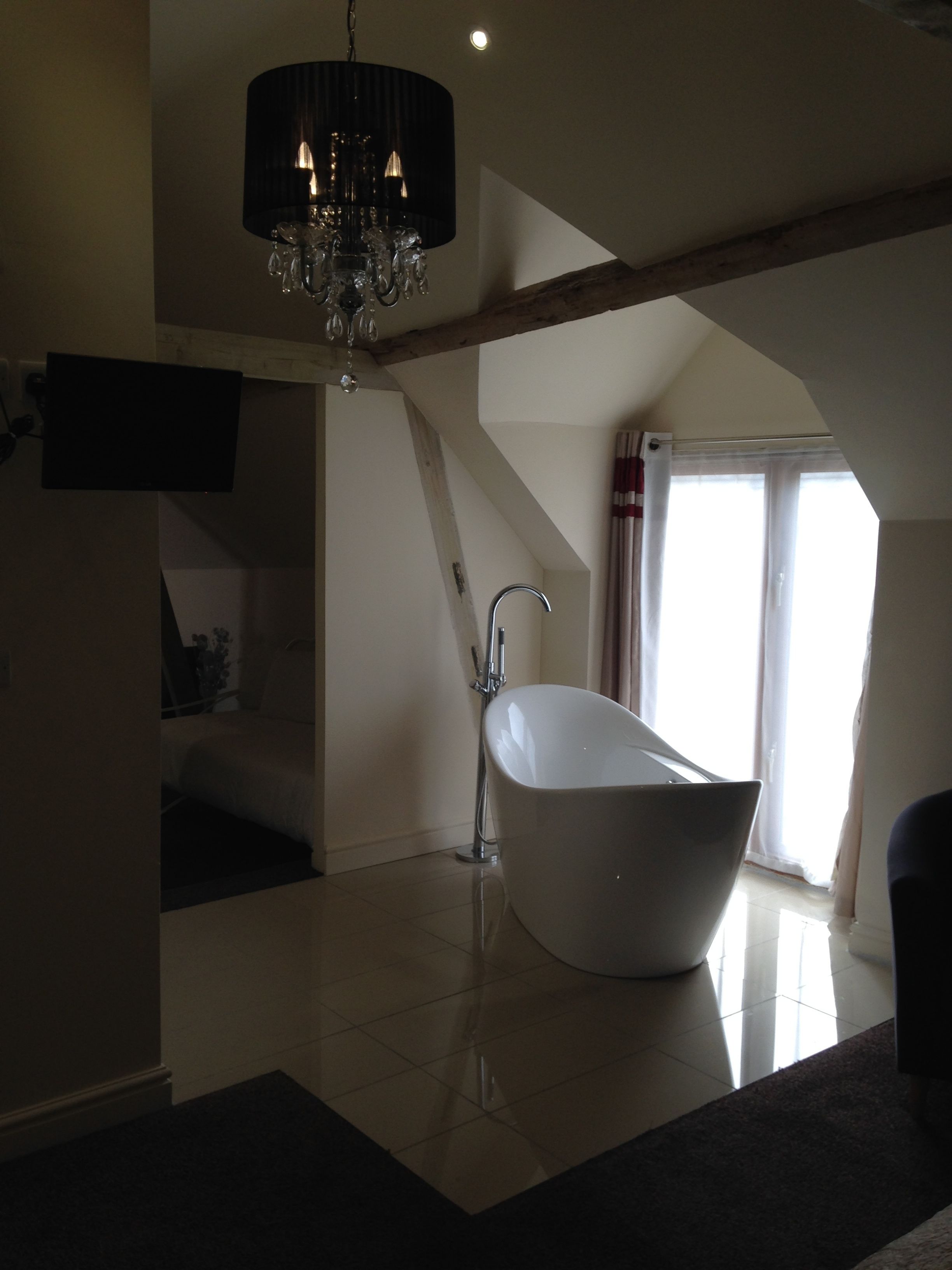 A spacious bathroom with a freestanding bathtub, a modern chandelier, and a large window providing natural light.