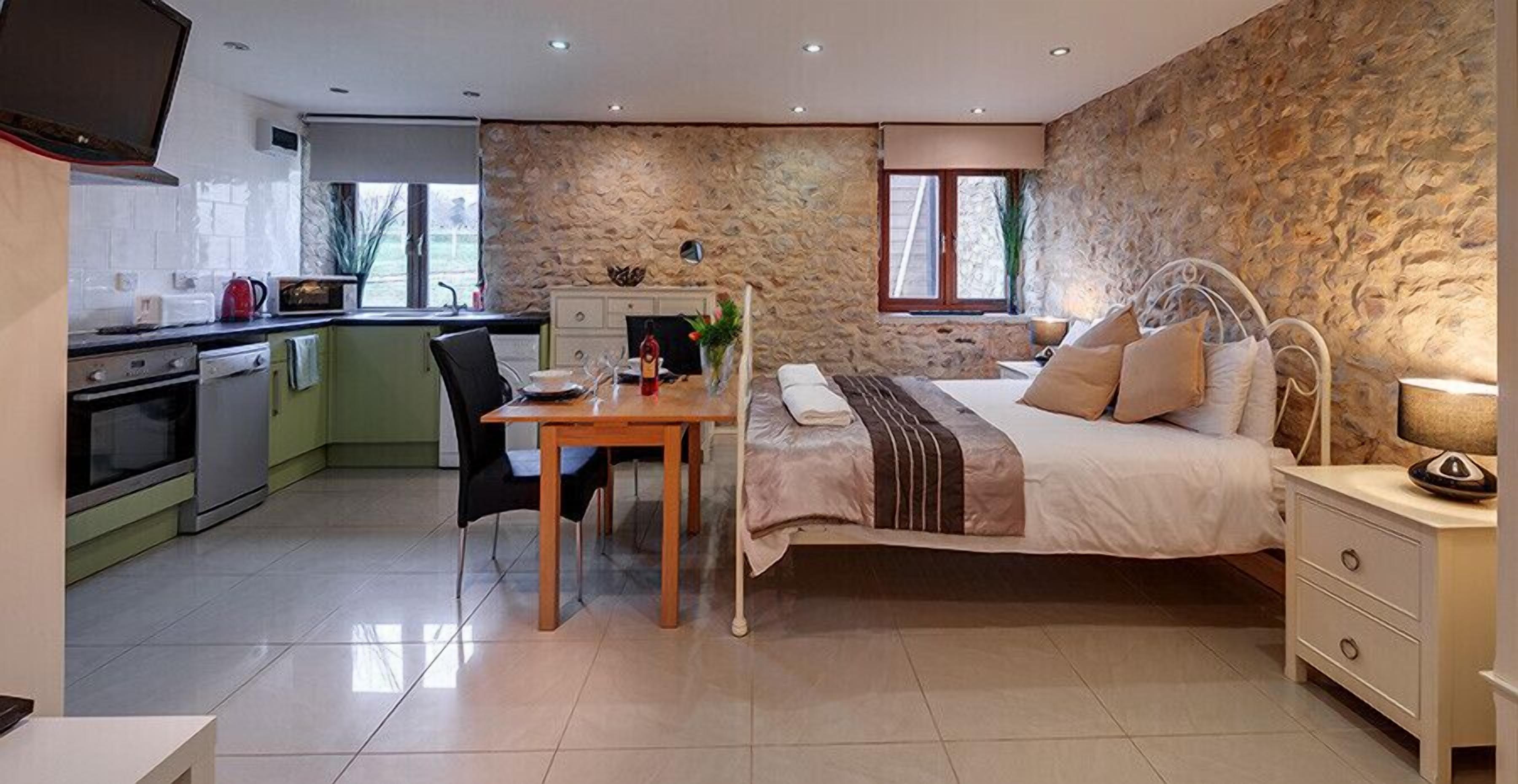 A compact bedroom with a bed, bedside table, and a view of the kitchen.