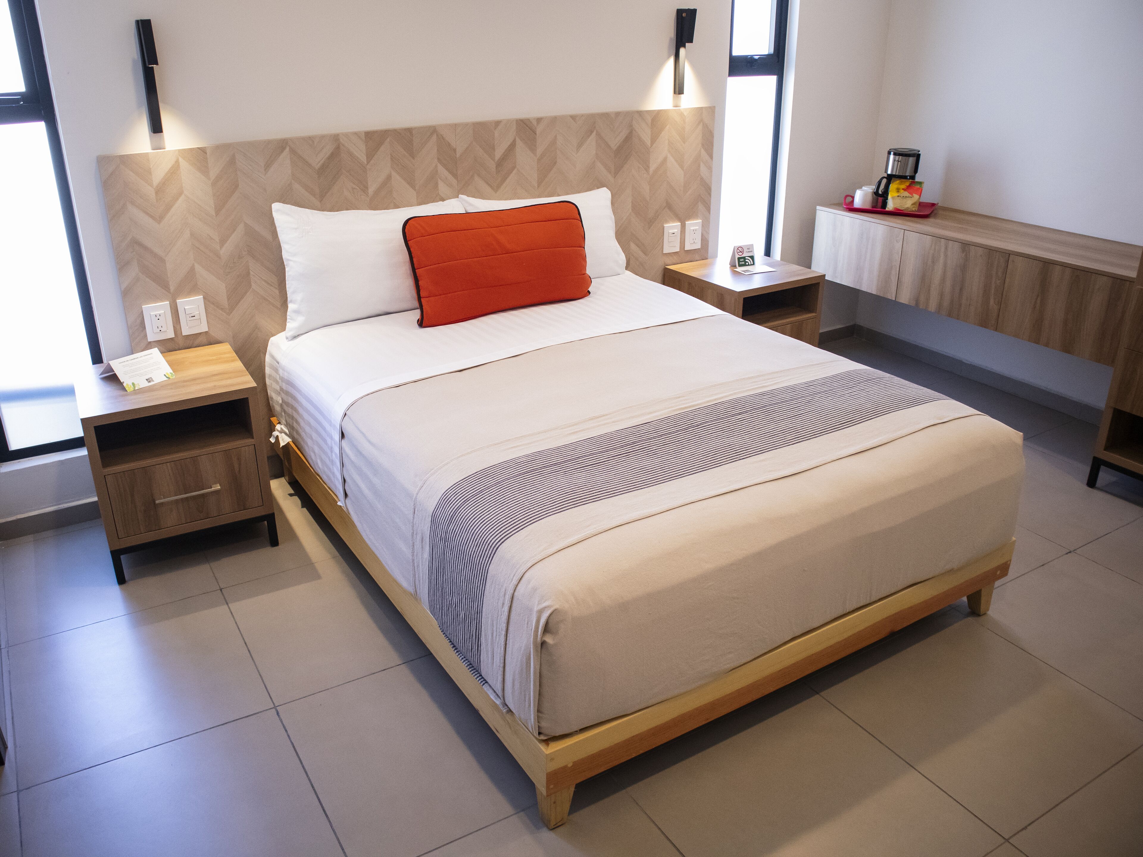 Ein modernes Hotelzimmer mit einem großen Bett, einem Holzkopfteil, Nachttischen und einem kleinen Beistelltisch.