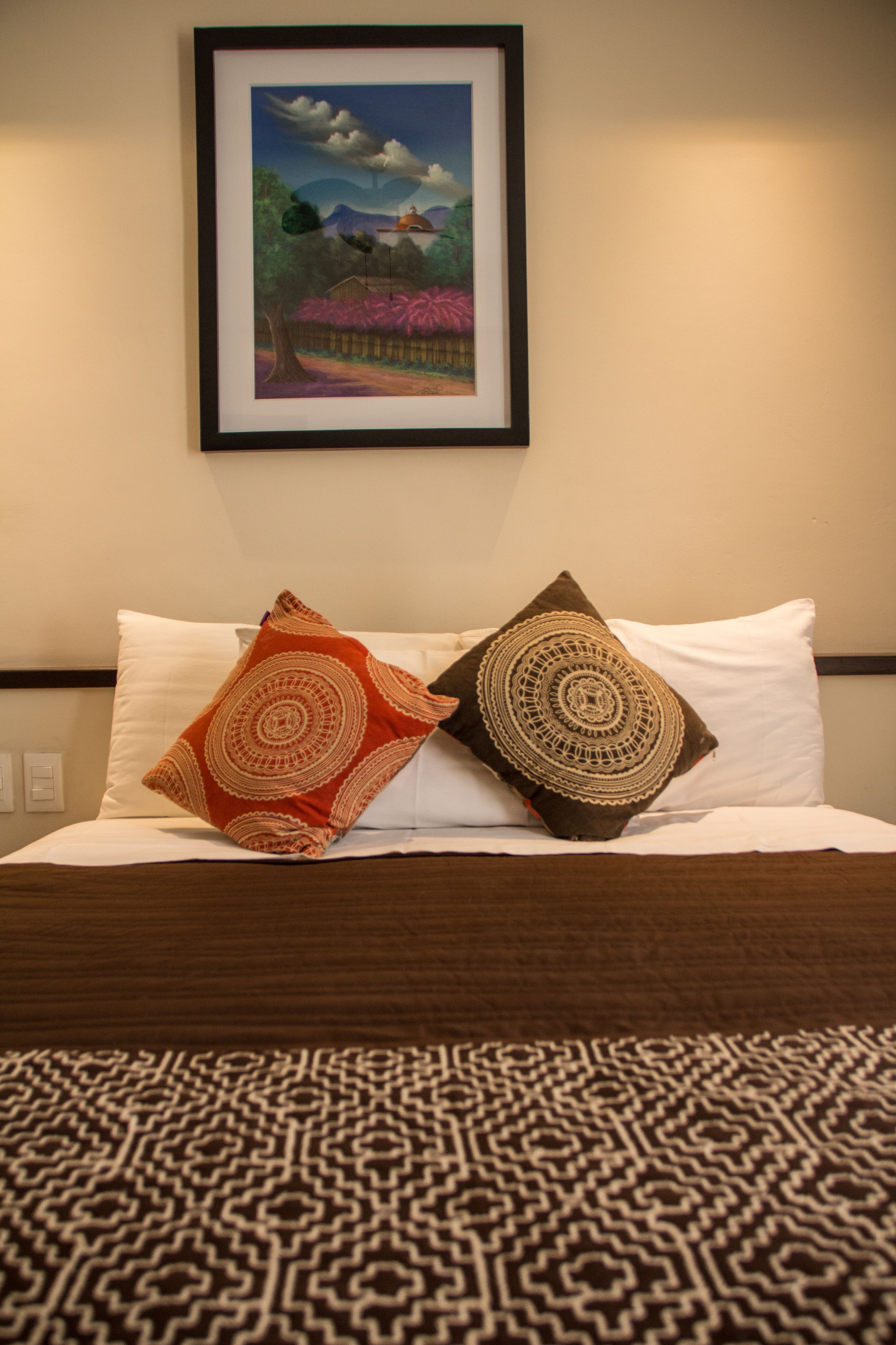 A neatly made bed with patterned bedding, a framed artwork above it, and a patterned rug on the floor.