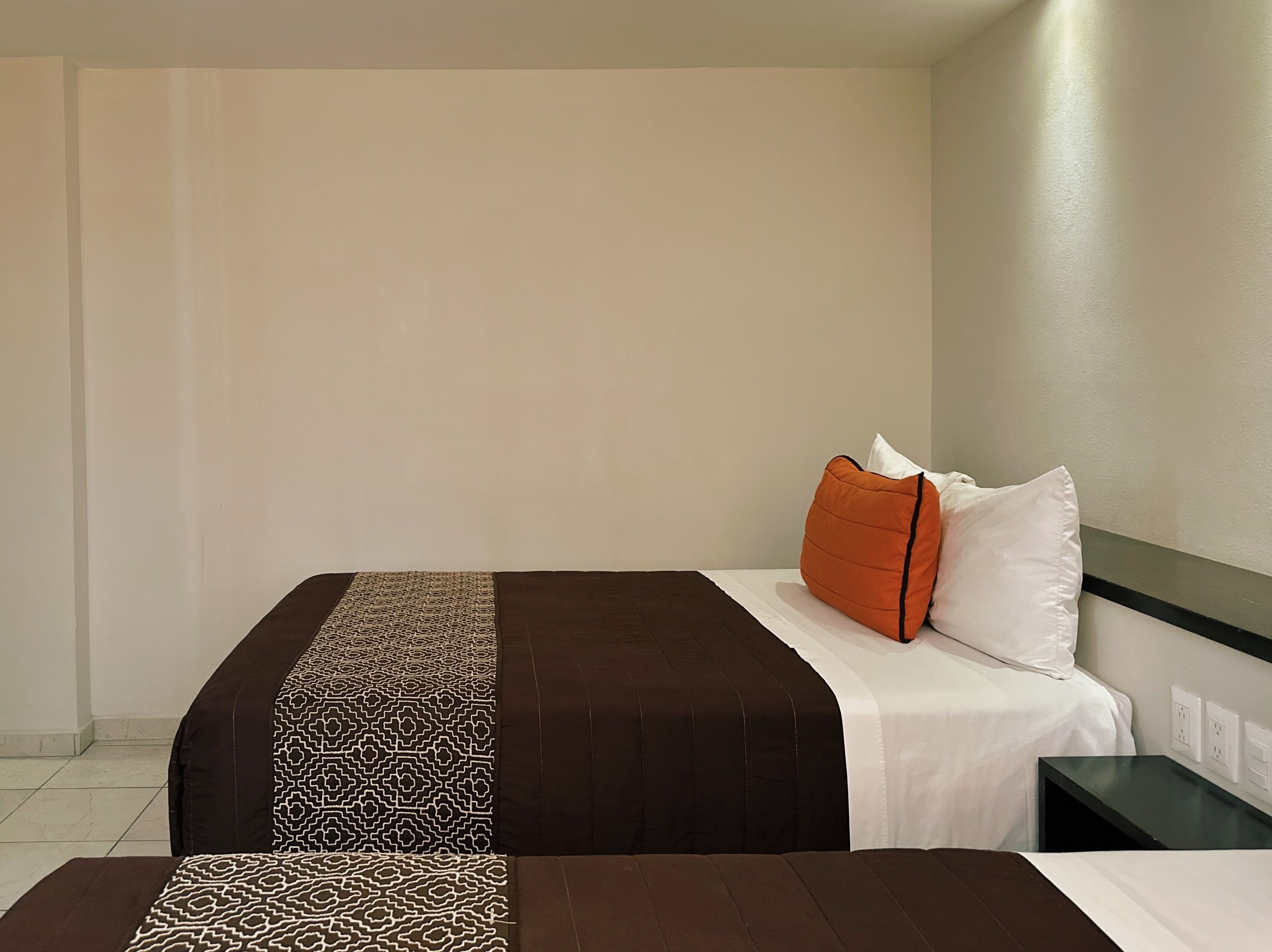 A hotel room with a bed, a nightstand, and a wall socket.