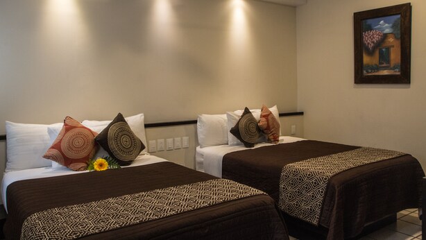 Habitación de hotel con dos camas, cada una con cubrecamas estampados y cojines decorativos.