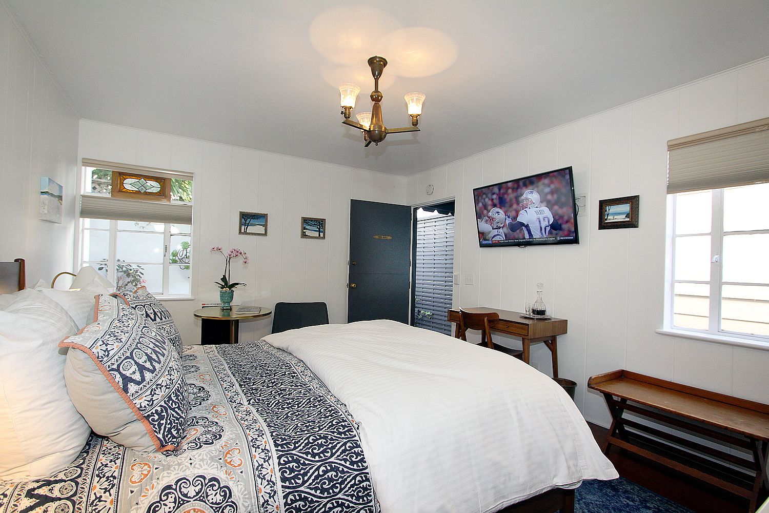 A hotel room with a large bed, a desk, a chair, a TV, and a window with blinds.