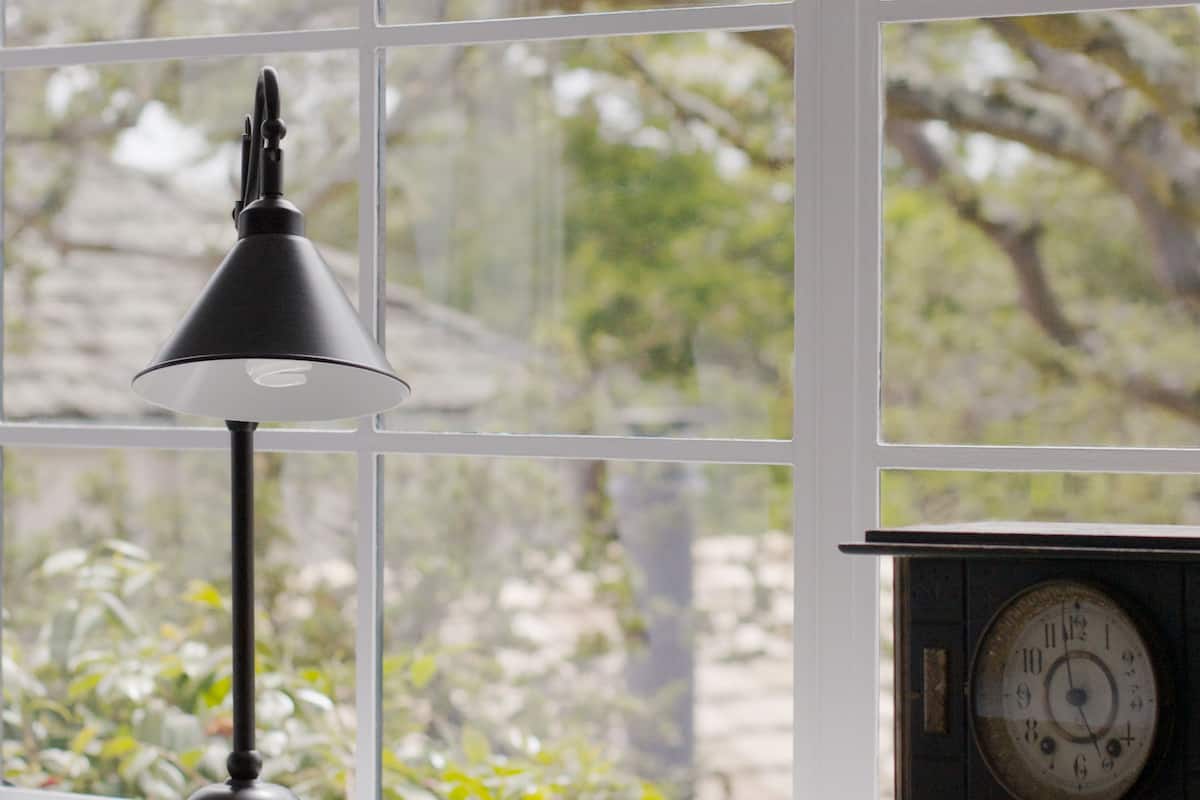 A desk with a lamp and a clock, positioned near a window with a view of trees.