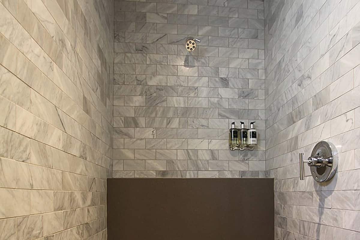 A modern shower with a marble wall and floor, a dark shower door, and a handheld showerhead.