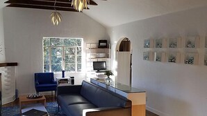 A living room with a fireplace, a blue sofa, a glass coffee table, and a television on a stand. - The Vagabond's House (Carmel)