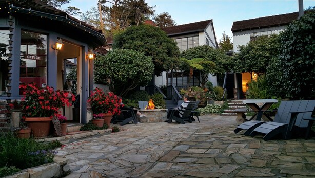 An outdoor patio area with stone flooring, potted plants, and a fire feature. - The Vagabond's House (Carmel)