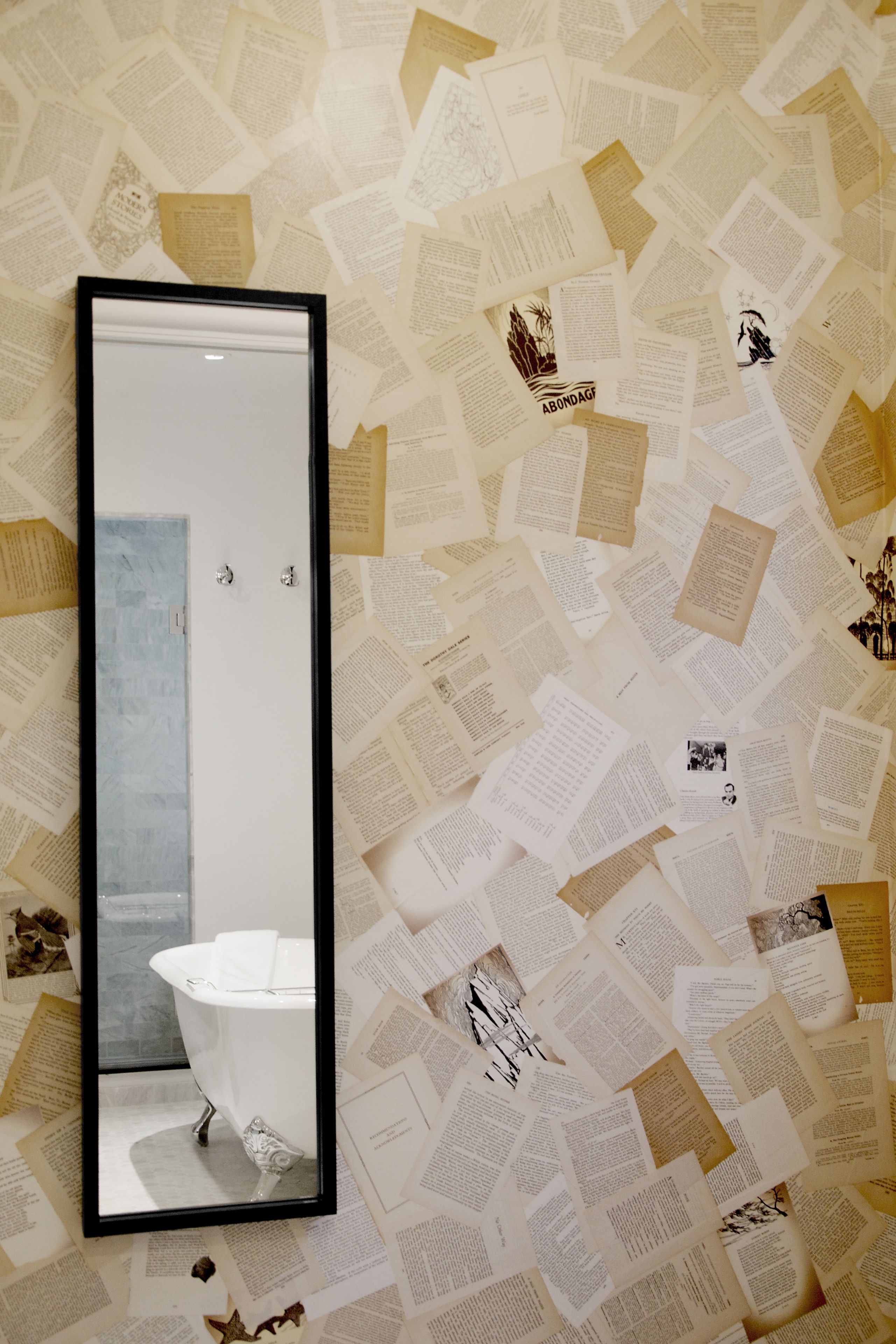 Een badkamer met een witte badkuip, een grote spiegel en een muur bedekt met bedrukte papieren.
