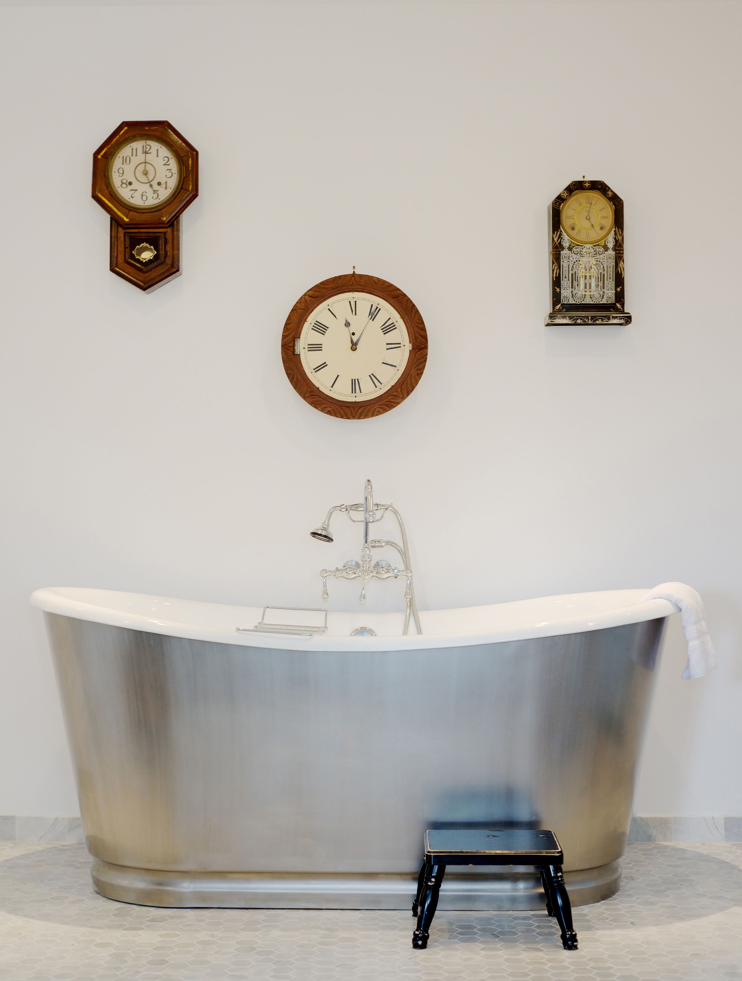 A bathroom with a freestanding bathtub, a wall-mounted clock, and a decorative clock.