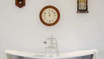 A bathroom with a freestanding bathtub, a wall-mounted clock, and a decorative clock.