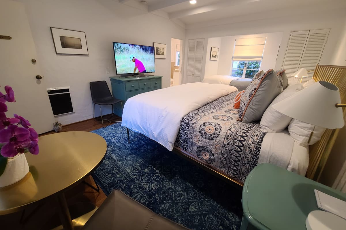 A hotel room with a bed, a TV, a desk, a chair, a small table, and a window.