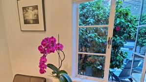 A room with a round table, two chairs, a potted orchid, and a framed picture on the wall. - The Vagabond's House (Carmel)