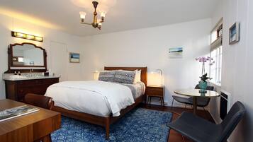 A hotel room with a bed, bedside table, chair, desk, and a small round table with a vase of flowers.