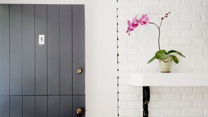 A grey door with a number plate and a white shelf with a potted plant and orchid. - The Vagabond's House (Carmel)