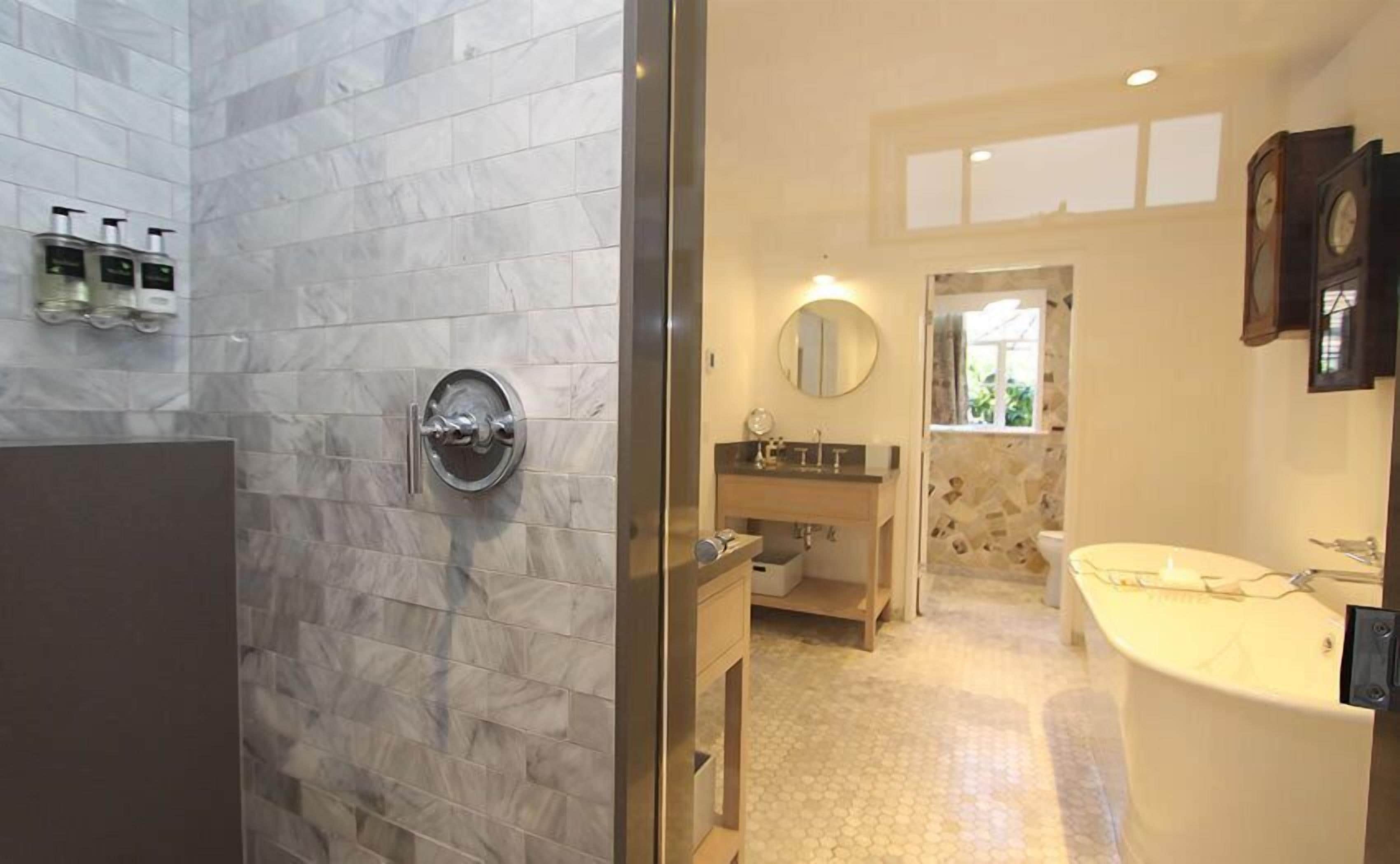 Une salle de bain avec un mur en marbre, un lavabo rond, un miroir et une horloge au mur.