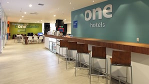 Een hotel receptie met een balie, barstoelen en een groot bord met de tekst 'one hotels'.