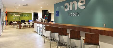 Zona de recepción de hotel con mostrador, taburetes de bar y un gran letrero que dice "one hotels".