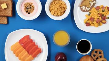 En frukostbuffé med rostat bröd, yoghurt, flingor, bönor, äggröra, korv, apelsinjuice, kaffe, äppelklyftor och bakverk.