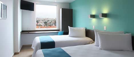 A hotel room with two beds, a large window with a city view, a flat-screen TV mounted on the wall, and a teal accent wall.