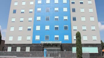 A multi-story hotel with a central blue section, a stone facade, and a gated entrance.