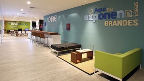 Een hotel receptie met een receptiebalie, een zithoek en een grote muur met de naam en slogan van het hotel.