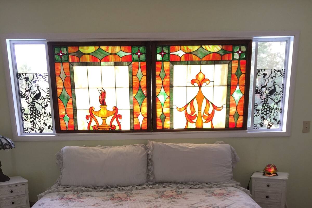 Et soveværelse med et blomstret sengetæppe, et natbord med en lampe og et vindue med farvet glas.