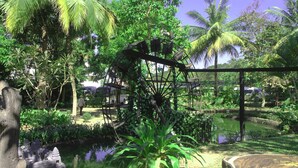 Un giardino tropicale con un elemento d'acqua, una struttura in legno e una vegetazione rigogliosa.