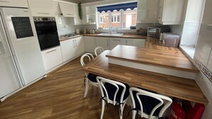 A modern kitchen with white cabinets, a wooden countertop, and a dining area with white chairs. - Parkside Guest House (Goole)