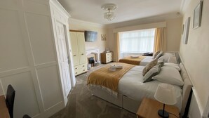 A hotel room with two beds, a television, a fireplace, and a large window with curtains. - Parkside Guest House (Goole)