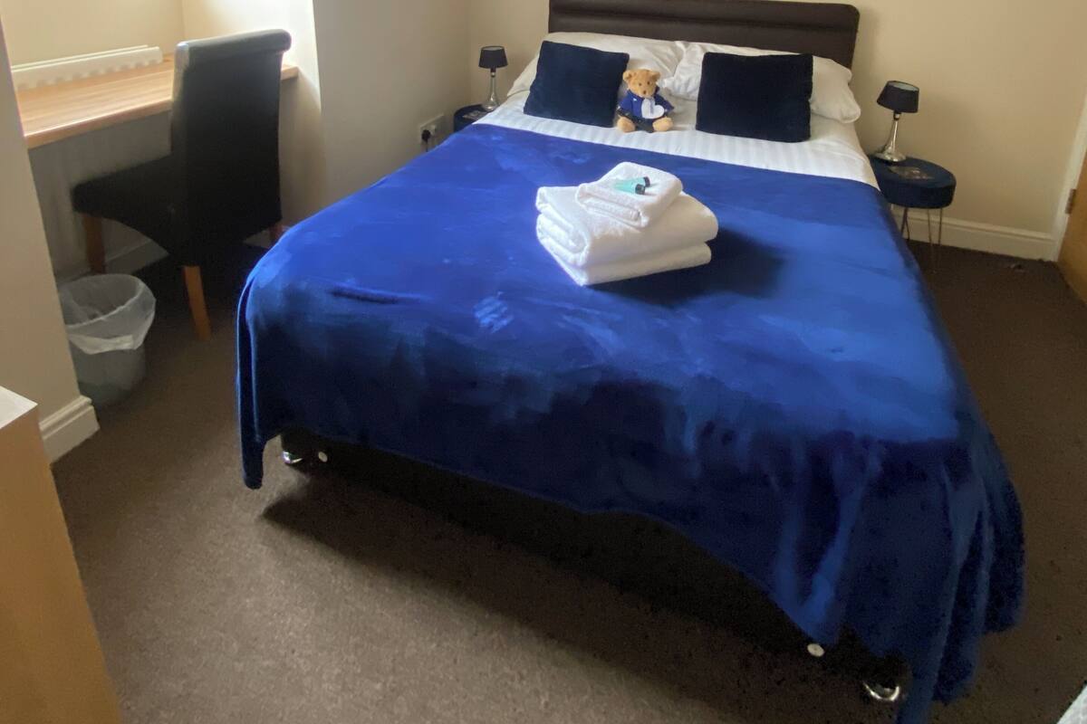 Une chambre à coucher avec un lit, un bureau, une chaise, une table de chevet et un tableau au mur.