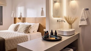 Una habitación de hotel moderna con cama, mesita de noche, tocador con espejo y un perchero para toallas.