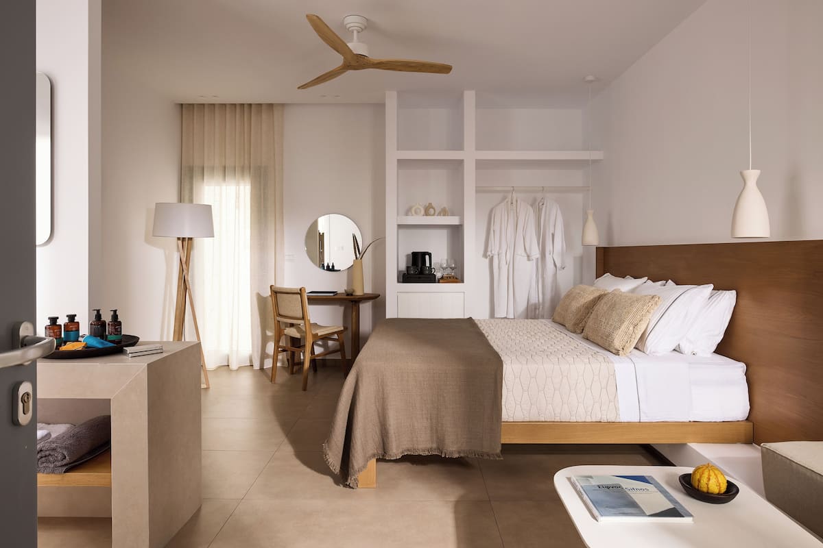 A modern hotel room with a bed, desk, chair, and a small table with a bowl and book.