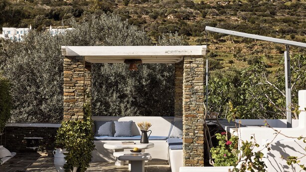 Un patio con paredes de piedra, una mesa blanca y una zona de estar con cojines.