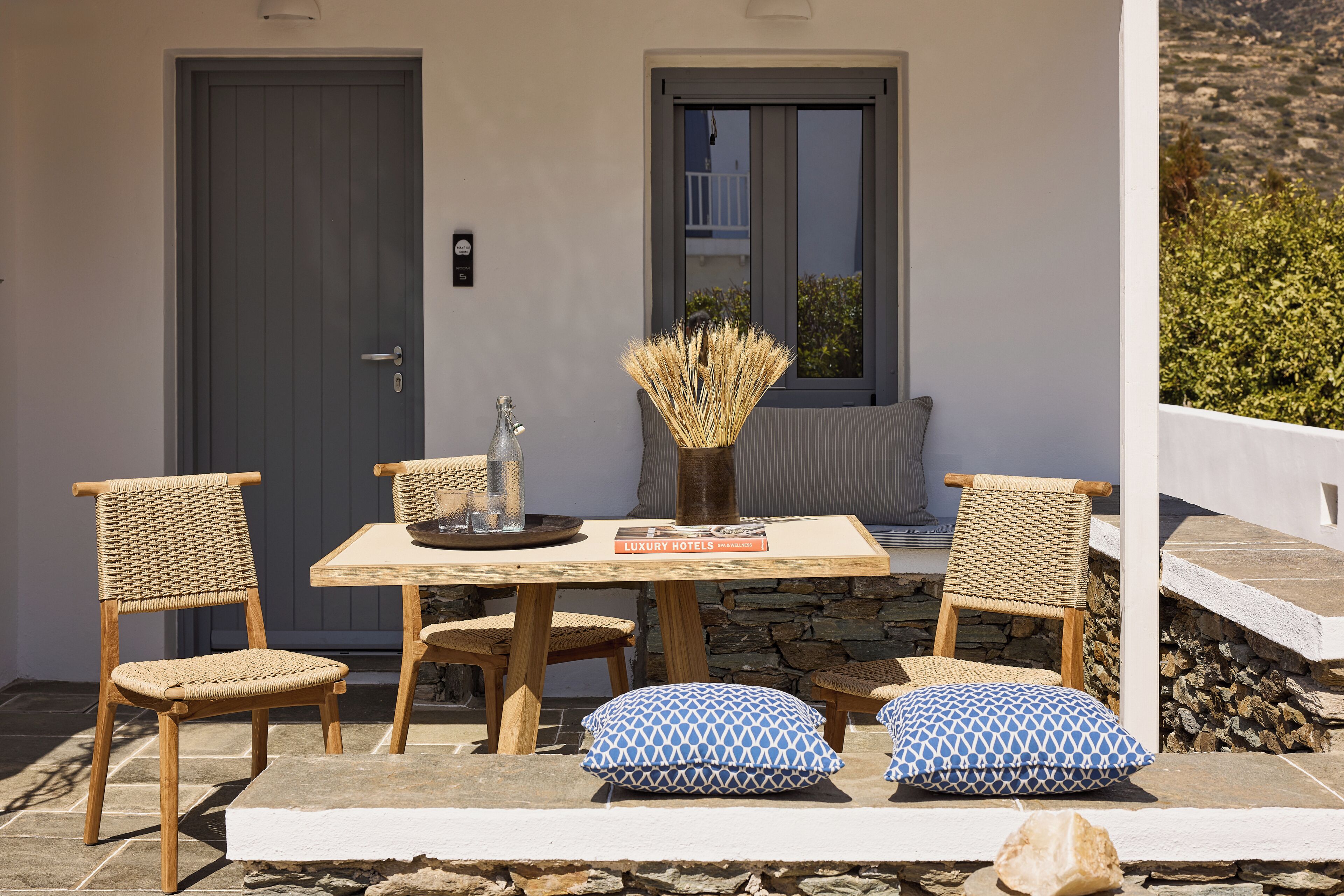 Un patio con una mesa, sillas, un libro y un jarrón con plantas secas.