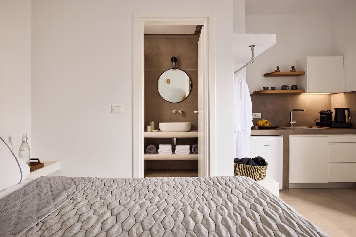 A modern hotel room with a bed, a bathroom with a sink and mirror, and a kitchenette.
