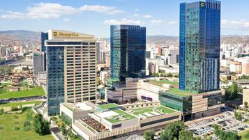 Un moderno complejo de edificios con un llamativo letrero del hotel 'Shangri-La', rodeado de otros edificios altos y una zona verde con parque.