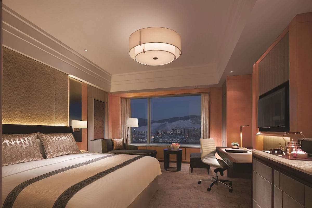 Een hotelkamer met een groot bed, een bureau, een stoel, een televisie en uitzicht op een stadsbeeld.
