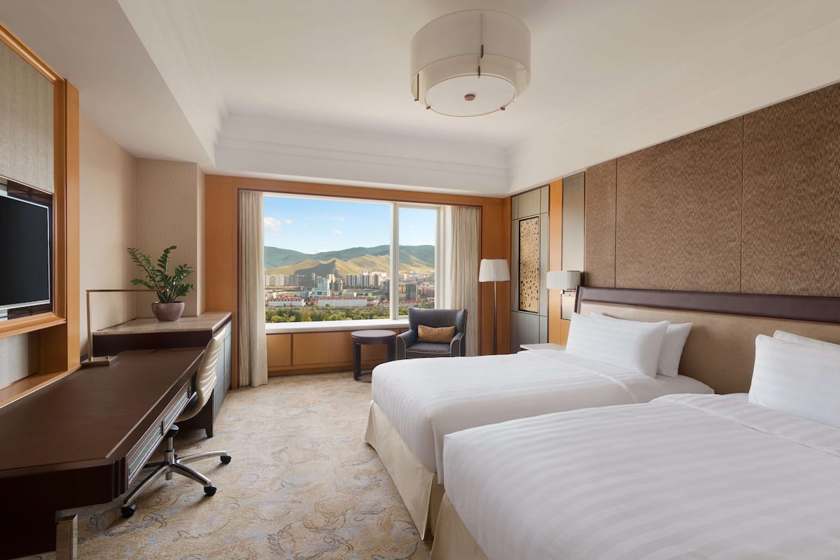 Een hotelkamer met een groot bed, een bureau, een stoel, een televisie en uitzicht op een stadsbeeld.