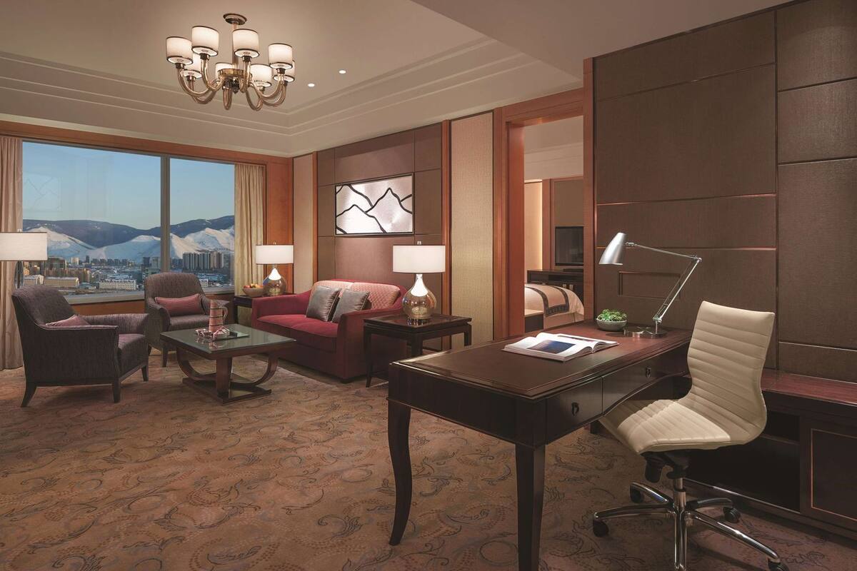Een hotelkamer met een groot raam, een kroonluchter, een bureau, een stoel, een bank en een bed.