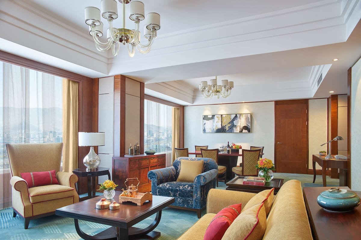 Een ruime hotellobby met een grote zithoek, een eettafel en een kroonluchter.
