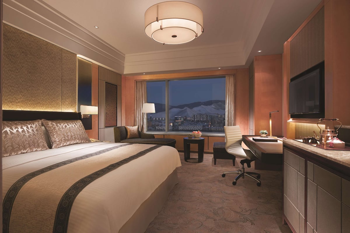 Hotelkamer met een groot bed, een bureau, een stoel, een televisie en uitzicht op een stadsbeeld 's nachts.