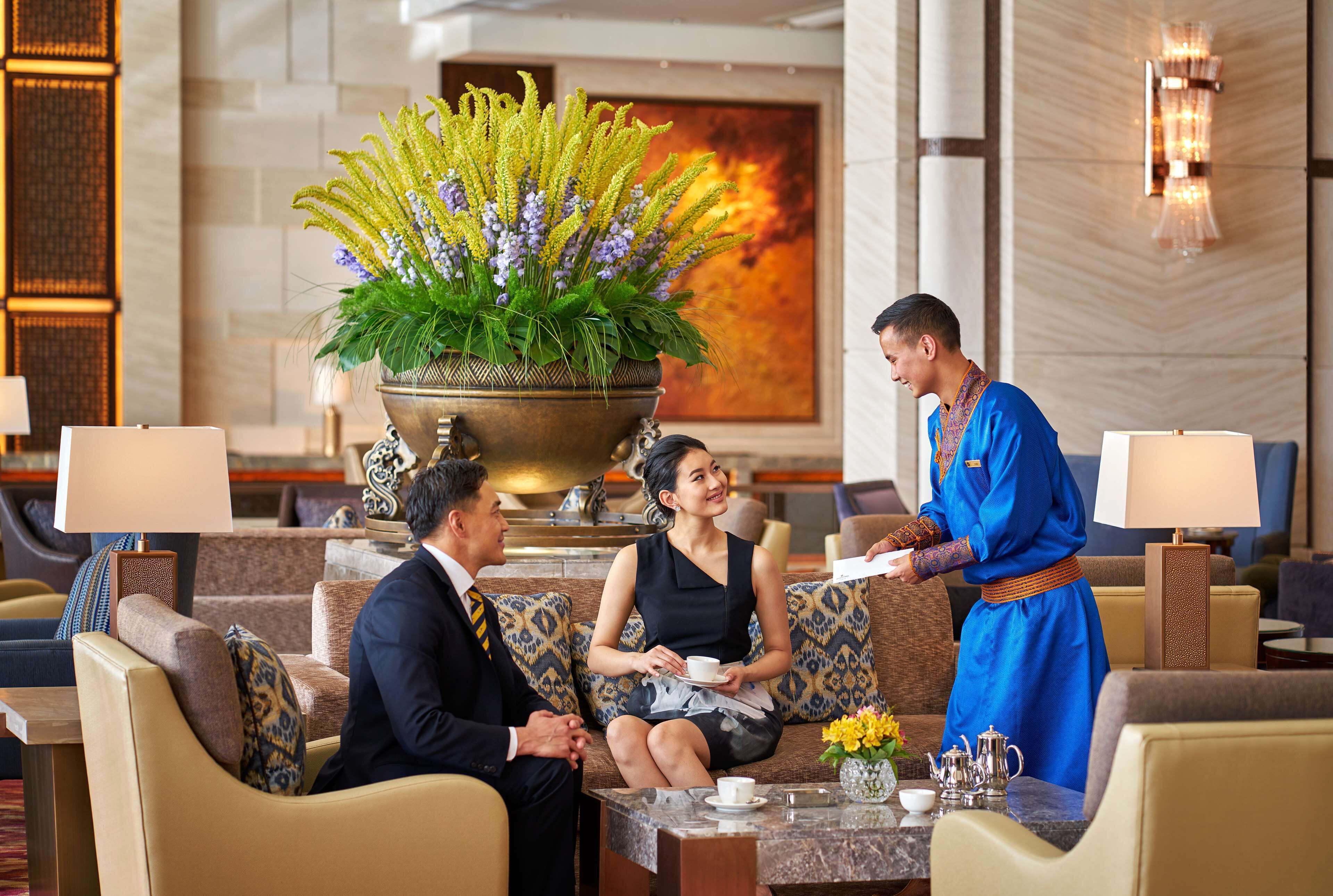 Un vestíbulo de hotel con una planta ornamental grande, asientos cómodos y una zona de recepción.