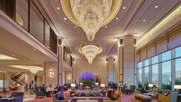 A spacious lobby with a large chandelier, comfortable seating areas, and a view of the outdoors through large windows.