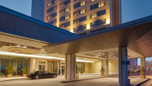 A high-rise hotel with multiple floors, a covered entrance, and a car parked in front.
