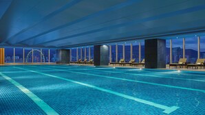 A large indoor swimming pool with lounge chairs and a city view.