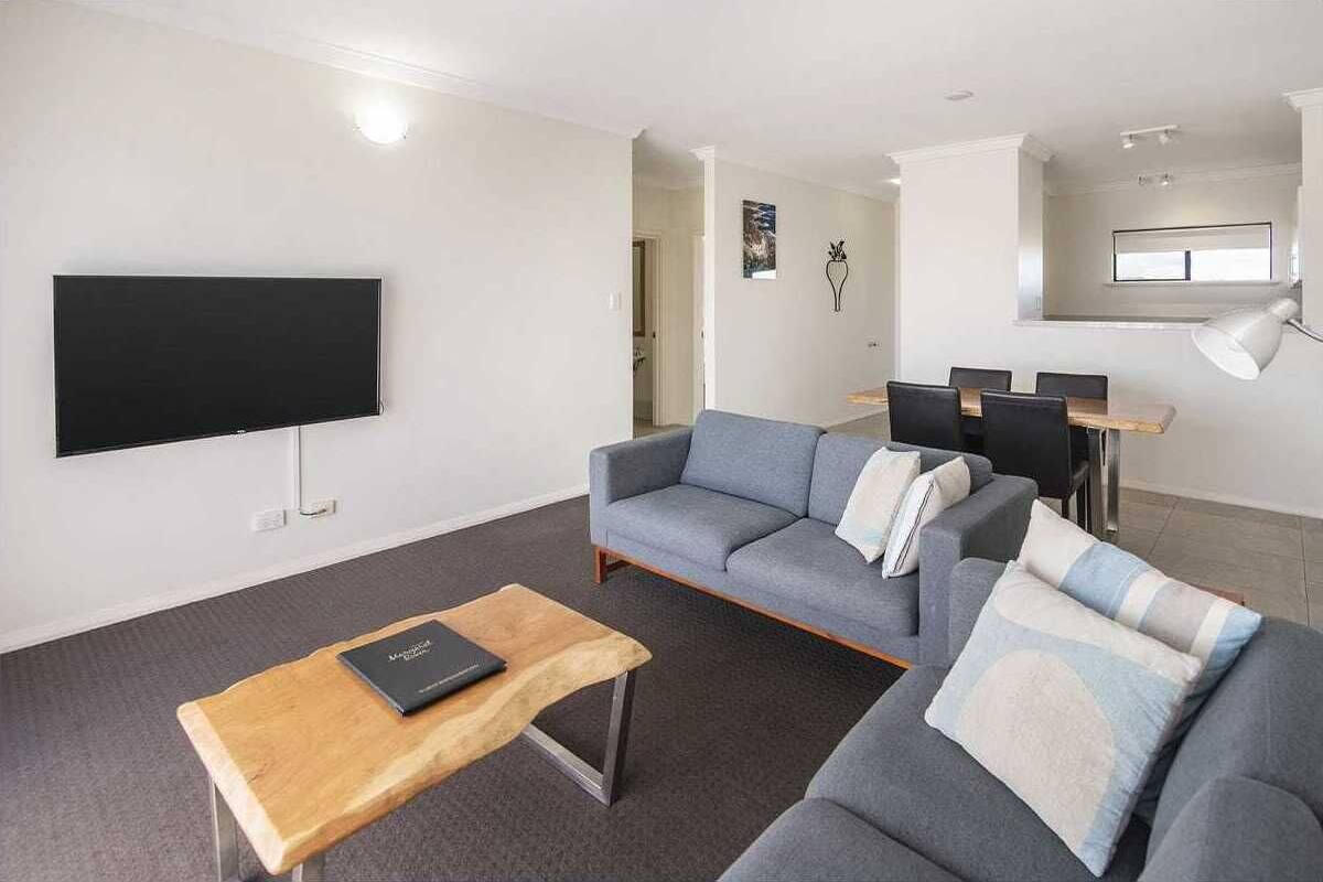 Ein modernes Wohnzimmer mit Flachbildfernseher, grauen Sofas, einem Holztisch und einem Essbereich mit Tisch und Stühlen.