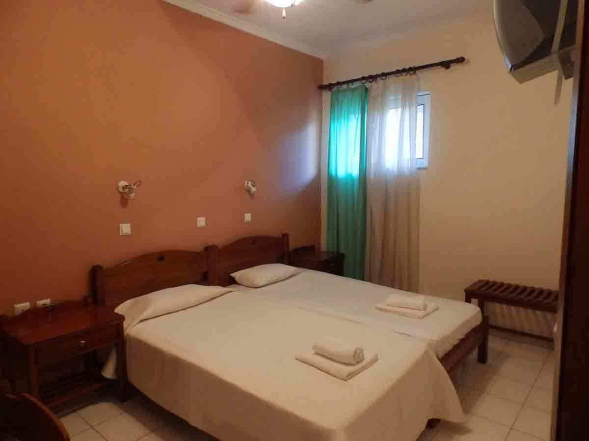 A standard hotel room with two beds, a wooden headboard, a small table, and a bench.