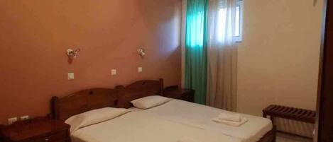A standard hotel room with two beds, a wooden headboard, a small table, and a bench.