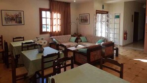 A dining area with tables and chairs, a sofa, and a window with curtains. - Alexandra Hotel (Chania)